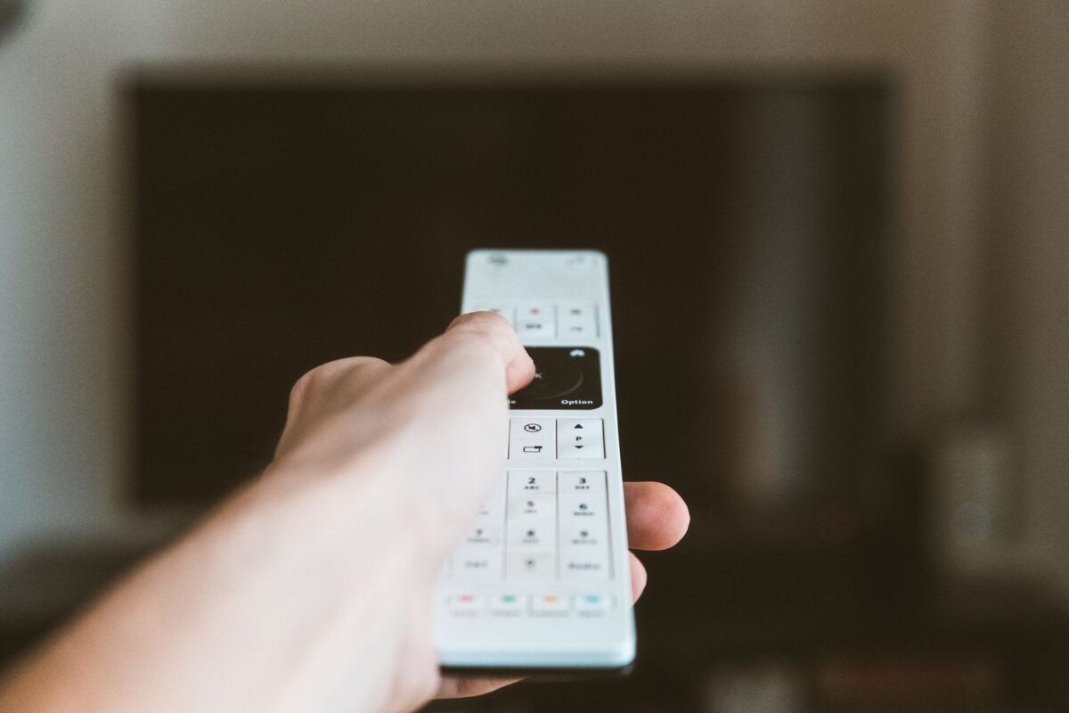 Main pointant une télécommande vers un téléviseur pour regarder France 2 en direct