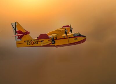 A Spanish firefighting plane soaring through a smoky sky at sunset, showcasing aerial firefighting.