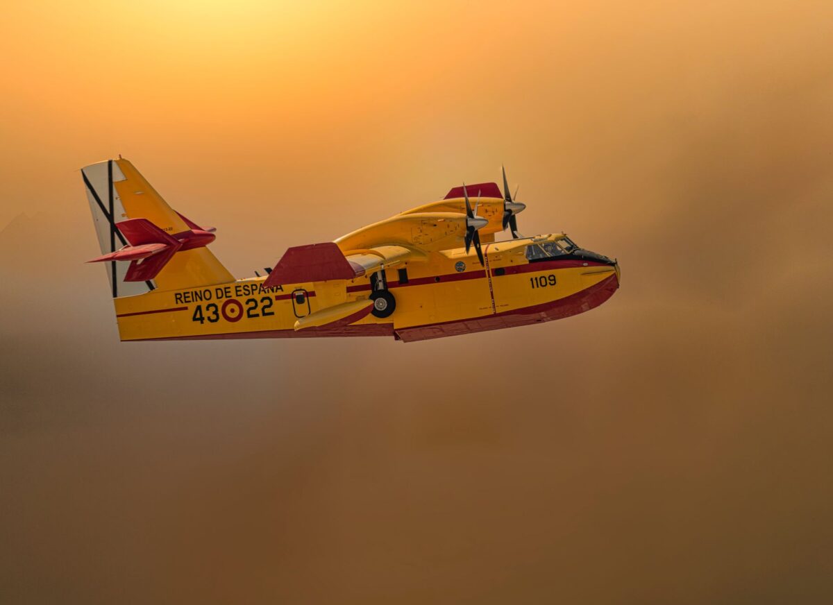 A Spanish firefighting plane soaring through a smoky sky at sunset, showcasing aerial firefighting.