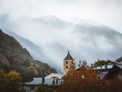 Scenic view of Ordino church tower amidst foggy mountains, capturing Andorra's enchanting landscape.