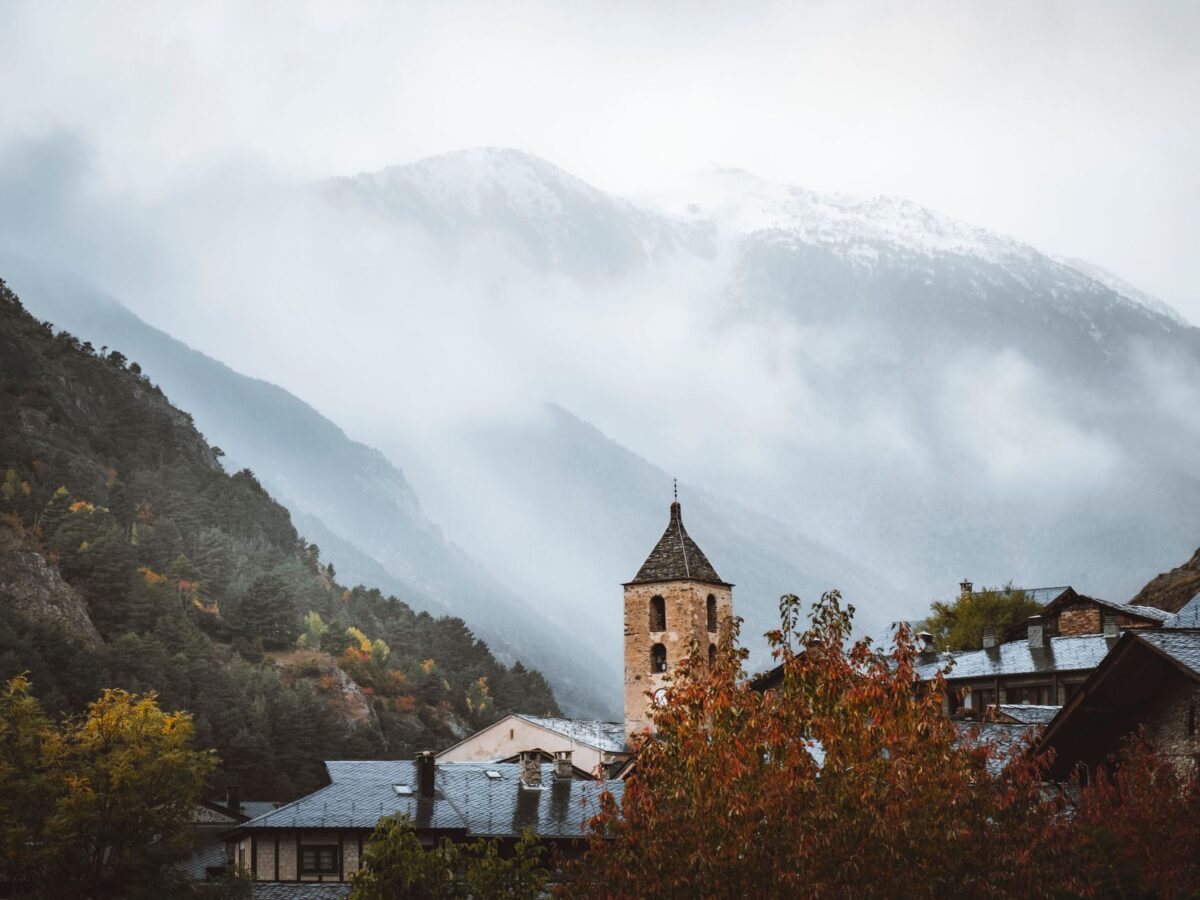 Scenic view of Ordino church tower amidst foggy mountains, capturing Andorra's enchanting landscape.