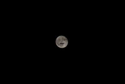An airplane silhouette against a bright full moon in a clear night sky, showcasing travel and exploration.
